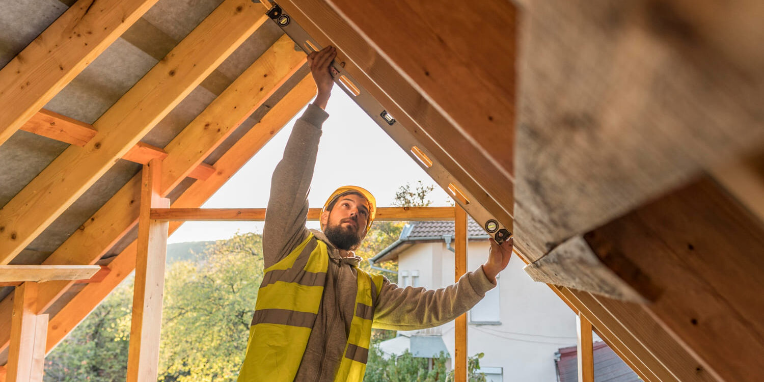 Bouwvakker controleert de dakconstructie tijdens een woninguitbouw met houten spanten.