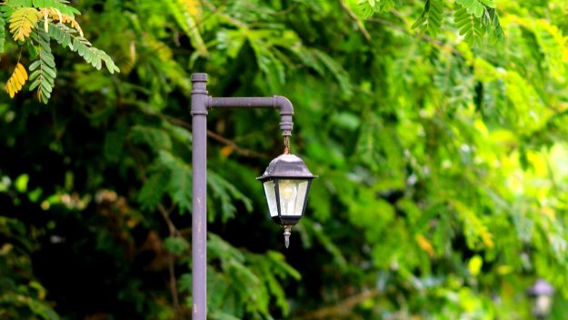 Verweerde buitenlamp in tuin Zwarte buitenlamp met verweerd armatuur in een groene tuin, symbool voor het belang van buitenlampen onderhouden.