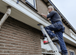 man op een ladder schildert een dakrand