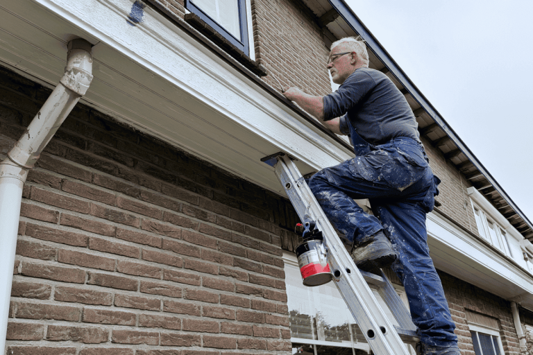 man op een ladder schildert een dakrand